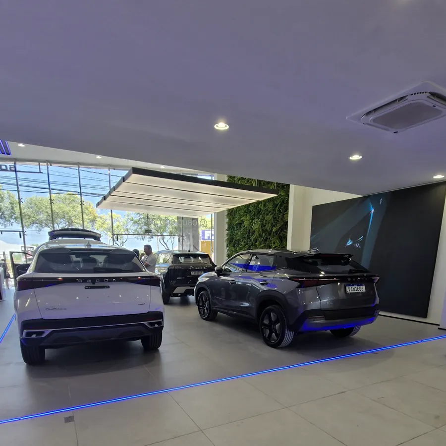 Entrada coberta da concessionária, com SUVs expostos junto à fachada de vidro