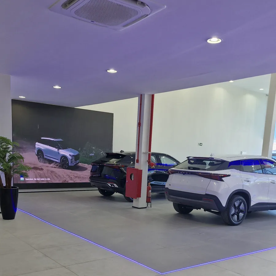 Salão de exposição com SUVs Omoda e Jaecoo sobre o piso com iluminação azul